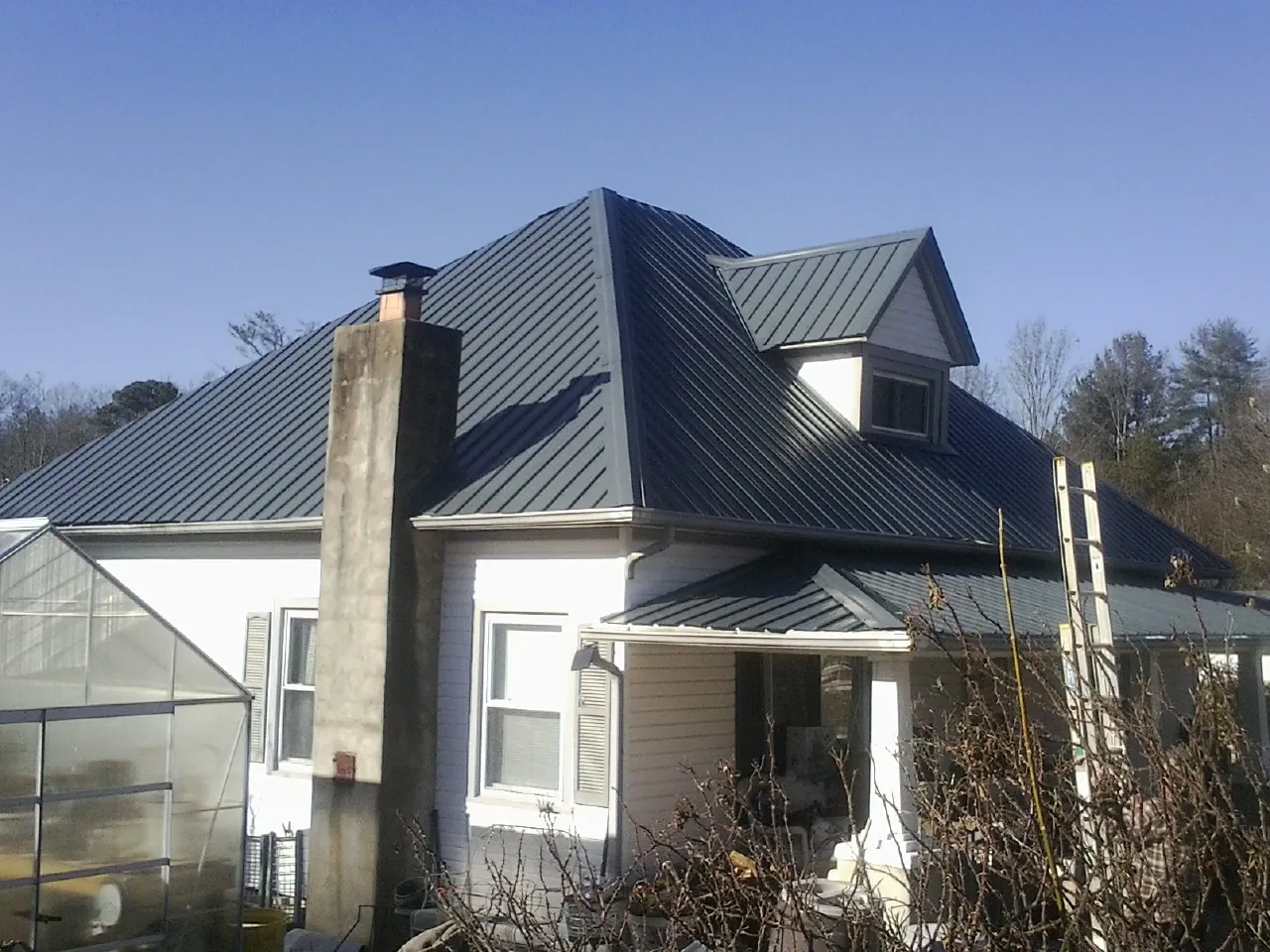 Dark blue standing seam metal roof on a white farmhouse with dormer — Slate & Tile Roof Repair by Roofing Brothers in Naytahwaush