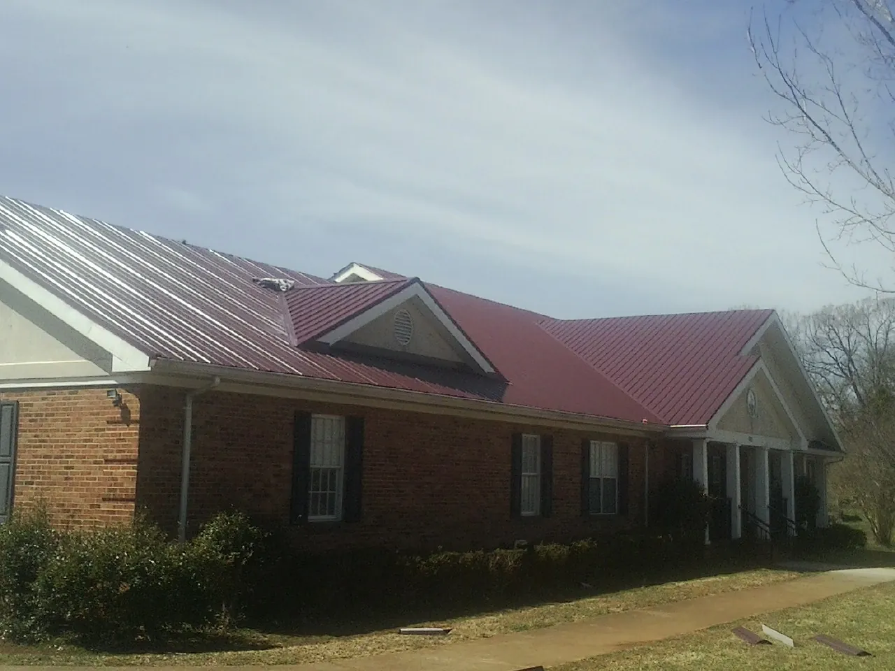Red metal roof with gabled entries on a long brick building, from a Hail Damage Roof Repair job in Naytahwaush