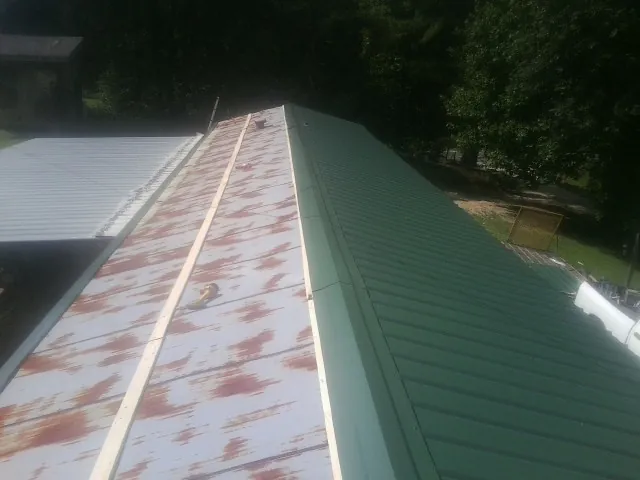 Old rusted panels beside newly installed green metal roofing — Wind Damage Roof Repair by Roofing Brothers in Naytahwaush
