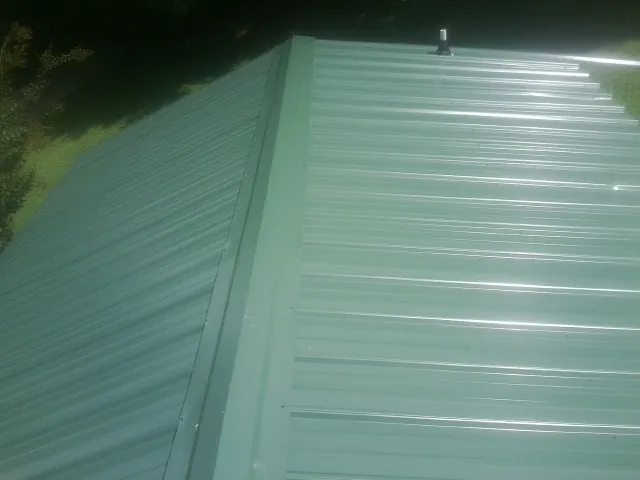 New green metal panels meeting at the ridge of a roof — Flat Roof Repair work by our crew in Naytahwaush