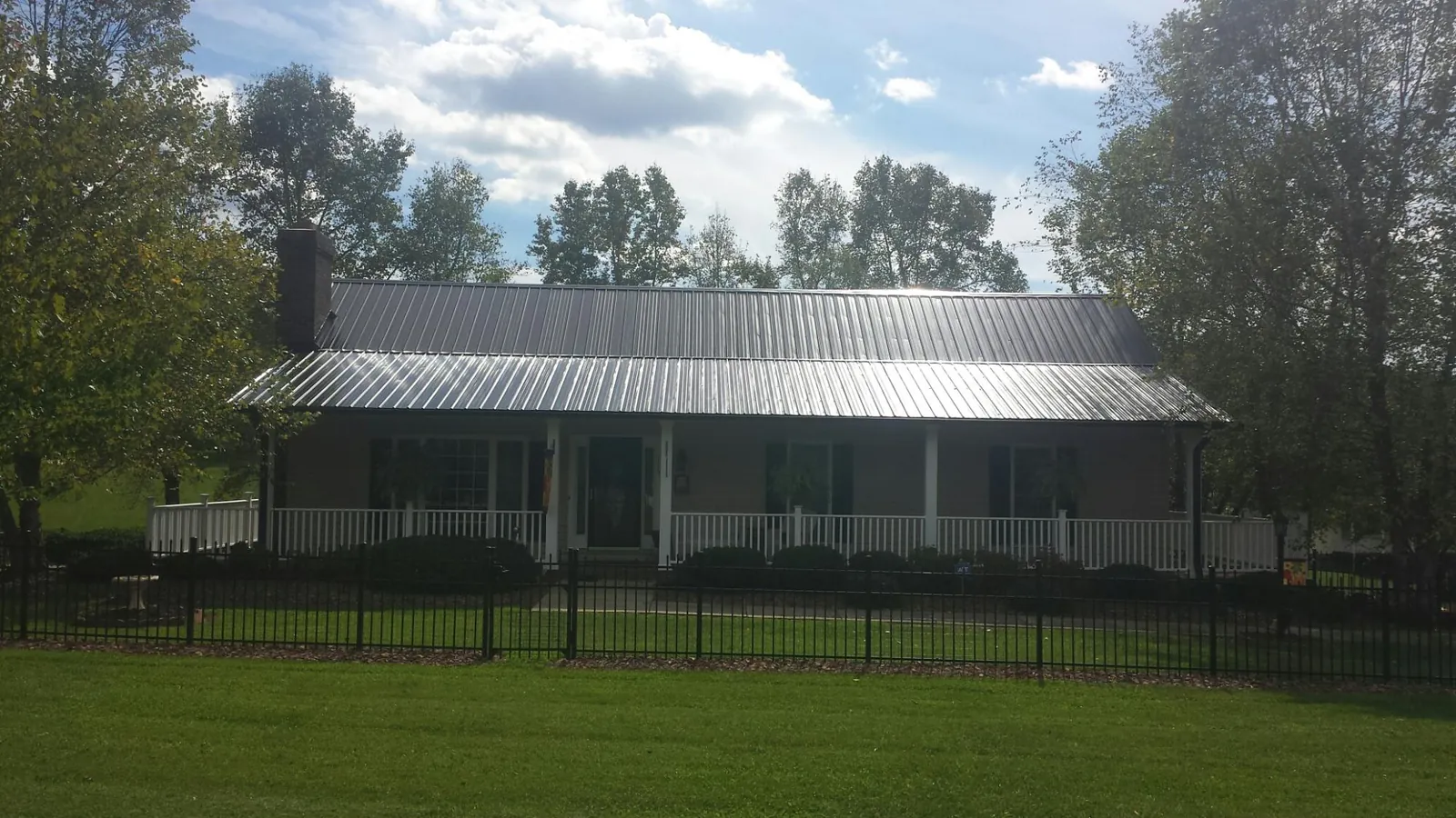 Gray metal roof on a brick ranch with a full width front porch — Gutter Guard Installation work by our crew in Naytahwaush