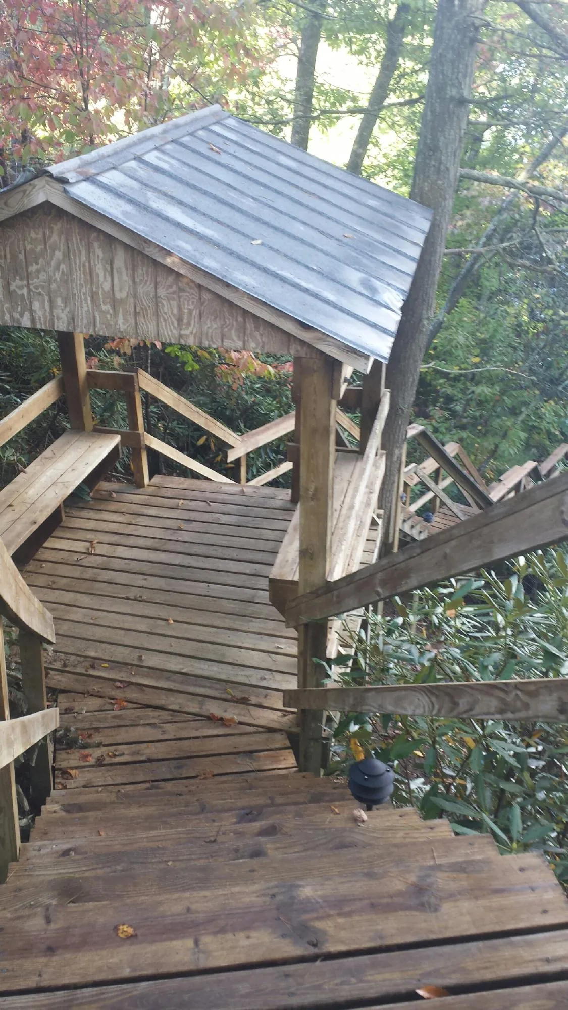 Metal roofed shelter over wooden steps on a wooded walkway — Skylight Repair & Installation work by our crew in Naytahwaush
