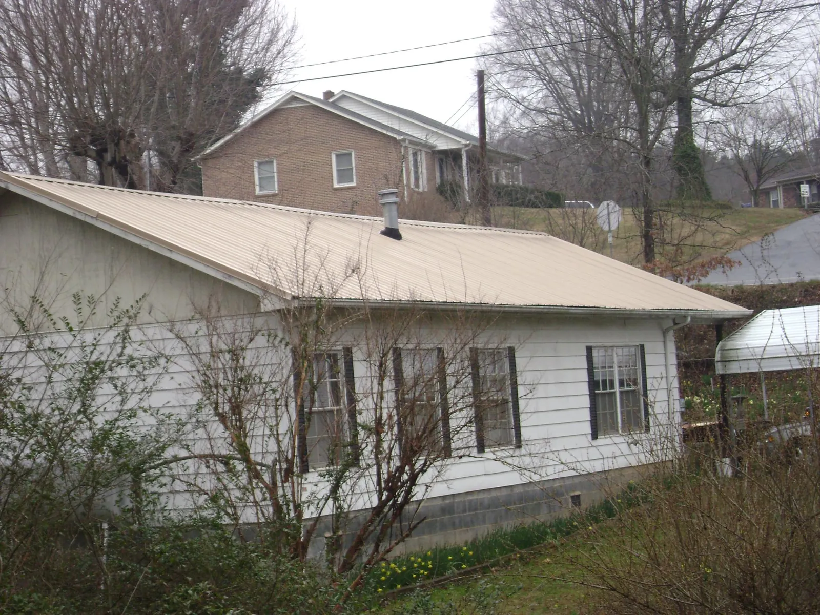 Tan metal roof on a white sided house set into a hillside — Commercial Roofing by Roofing Brothers in Naytahwaush