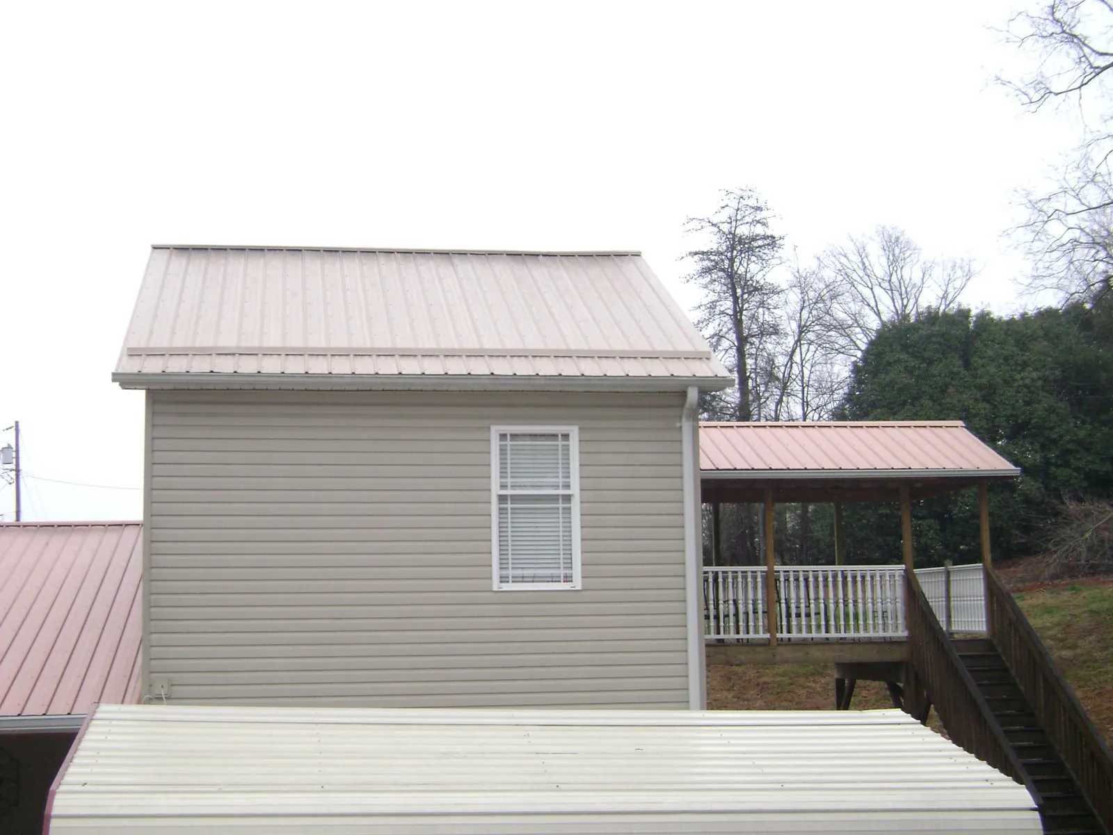 Tan metal roofs on a two story addition and attached porch, from a Roof Replacement job in Naytahwaush